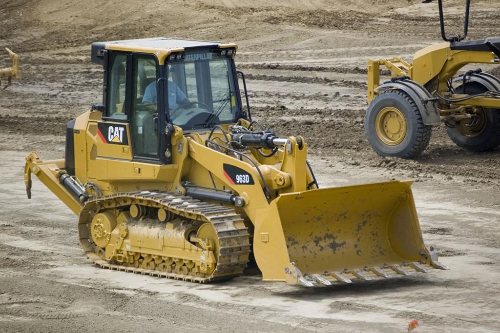 Carregadeira de esteira Caterpillar 963D amarela em operação em terreno de terra batida.